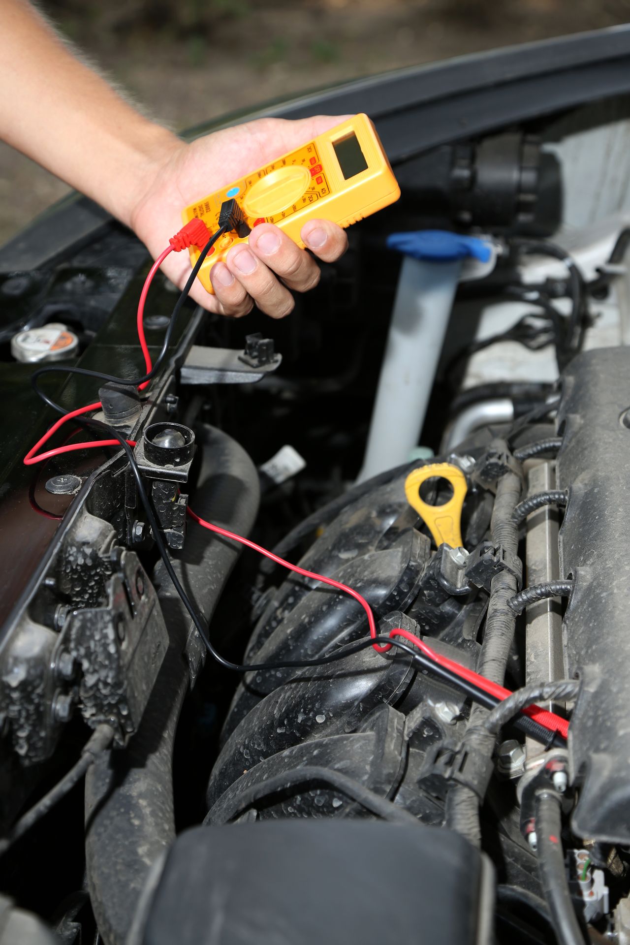 Atelier automobile : diagnostic électronique et contrôle de batterie sur voiture hybride, technicien vérifiant tension.