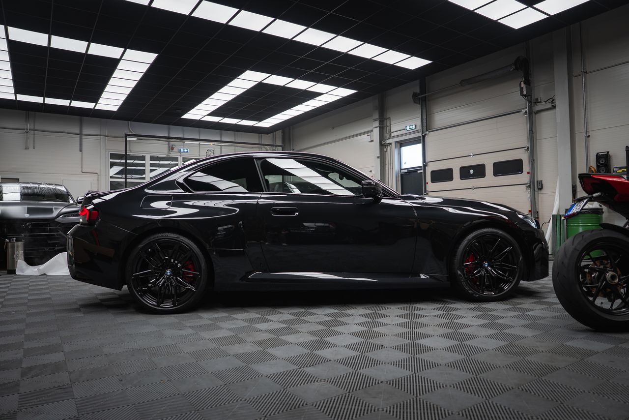 BMW M2 noire avec film PPF invisible protégeant capot et pare-chocs dans atelier detailing professionnel.
