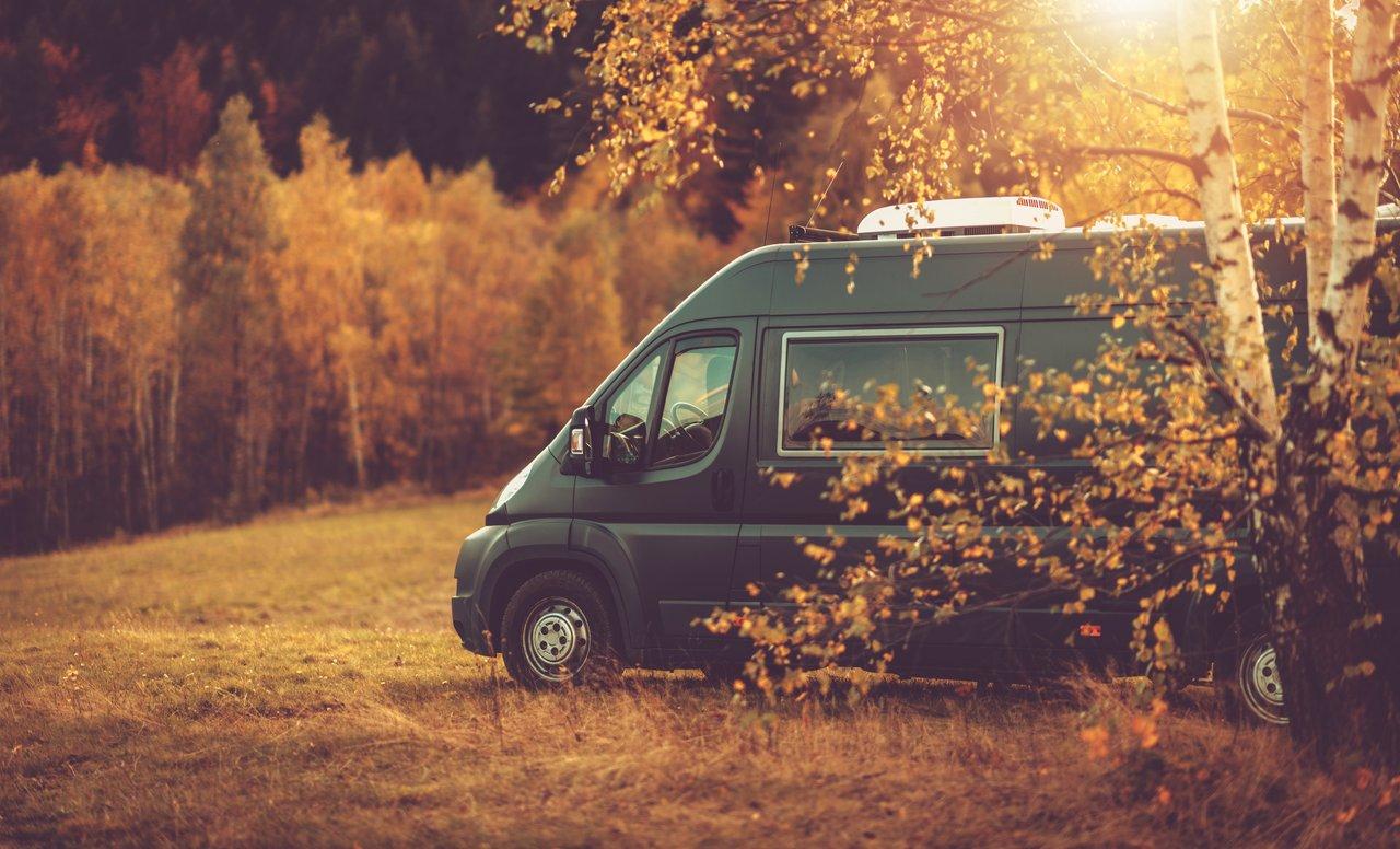Camper van en automne au bord d’un lac paisible entouré de montagnes colorées.