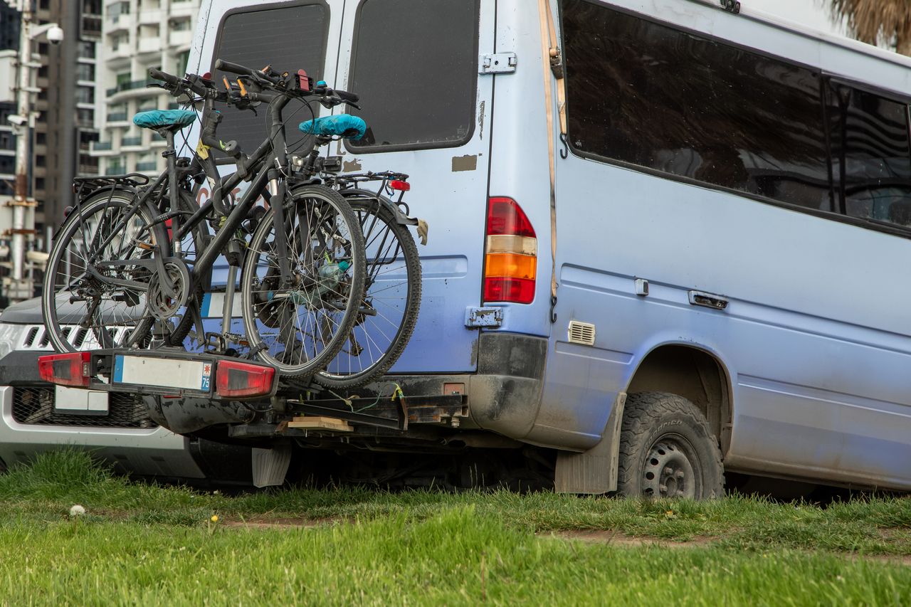 Camping-car light blue discret en ville près d’un panneau ZFE, vélos montés sur porte-vélos arrière.