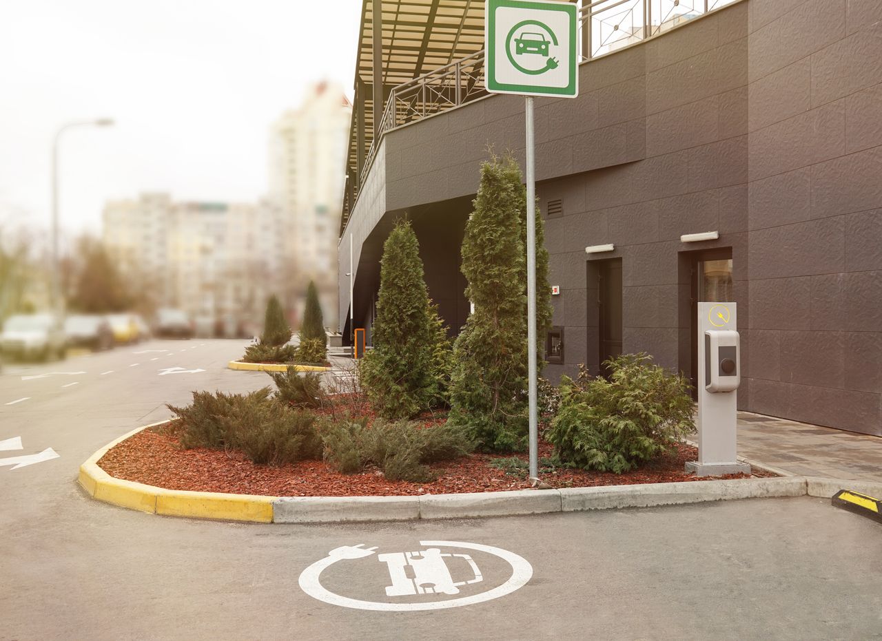 Citadine électrique compacte en ville, vue trois quarts avant, station de recharge urbaine lumineuse et moderne.