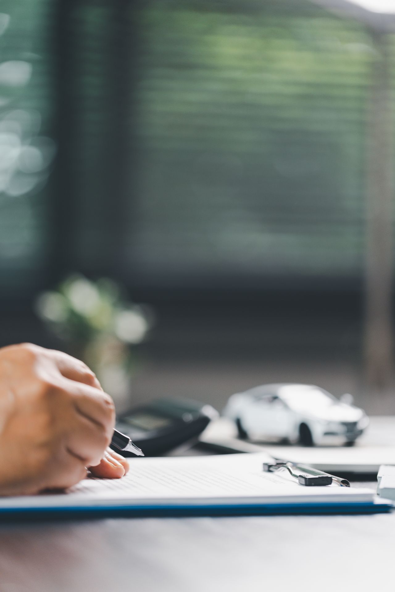 Client signe contrat de financement dans showroom moderne, clés posées sur table à côté du véhicule neuf