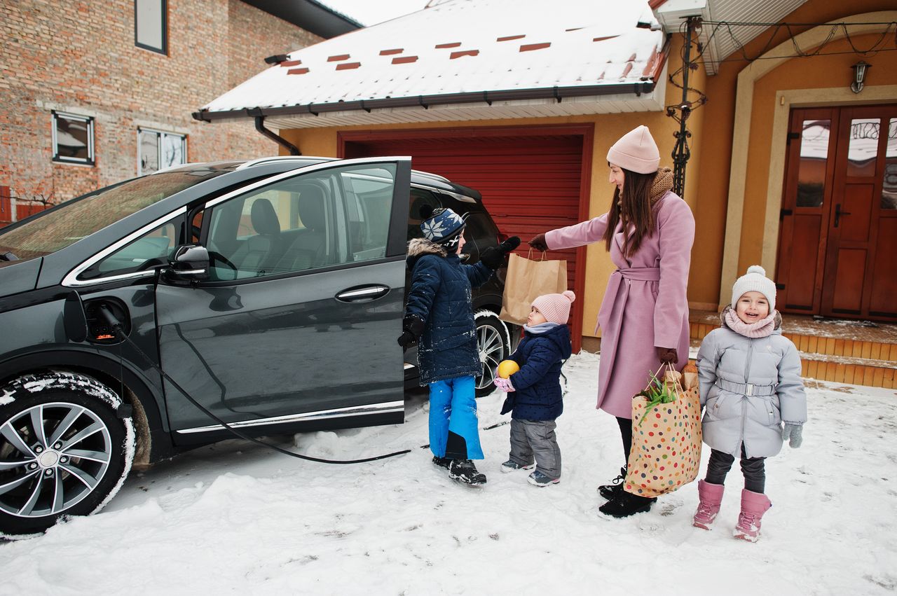 Comparatif de cinq SUV électriques 7 places devant une maison familiale, recharge et mode de vie durable.