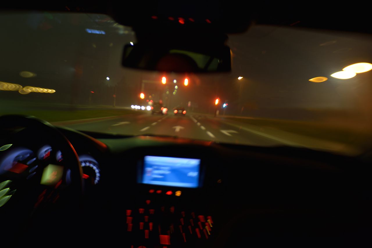 Conducteur fatigué sur autoroute de nuit, tableau de bord lumineux et circulation urbaine floue, ambiance réaliste.