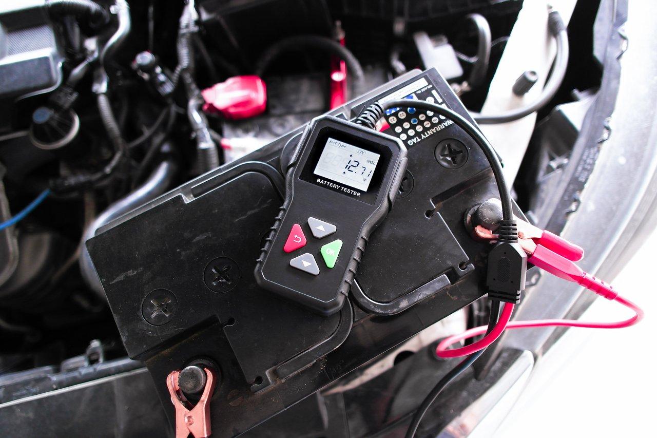 Contrôle de la batterie de voiture avec un voltmètre pour assurer une bonne préparation avant la rentrée.