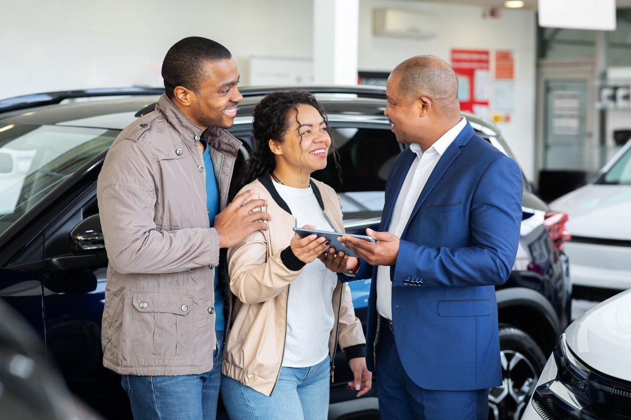 Couple noir découvrant leur parcours digital car buying journey avec un concessionnaire dans un showroom moderne.