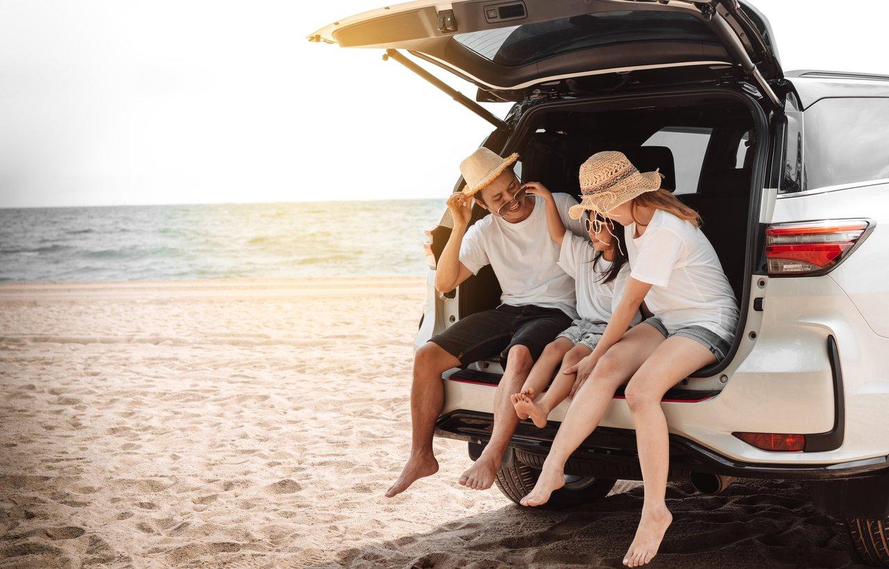Famille heureuse en voiture avec bagages sur le toit, prête pour des vacances d’été 2025.