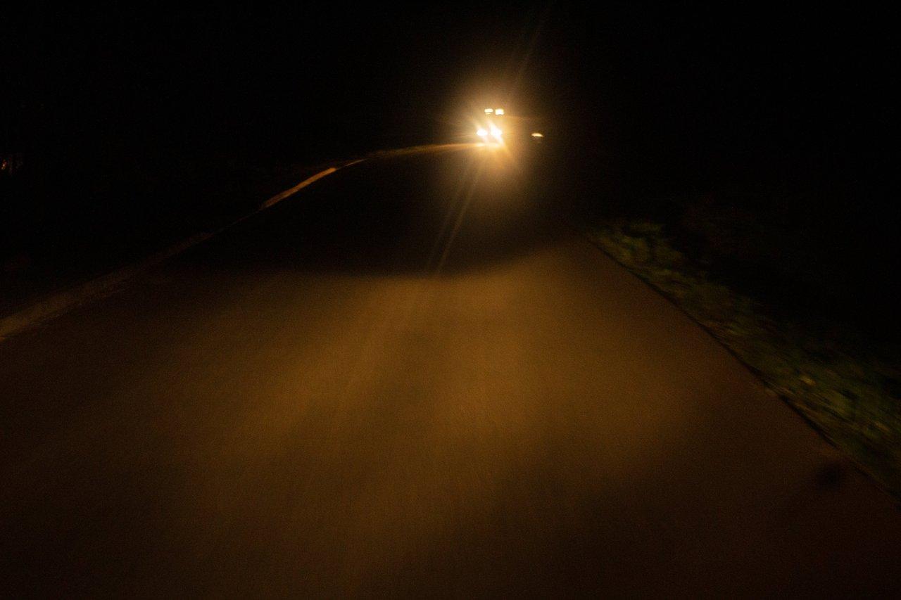 Feux de véhicule allumés la nuit sur une route rurale en période printanière, essentiel pour la sécurité.