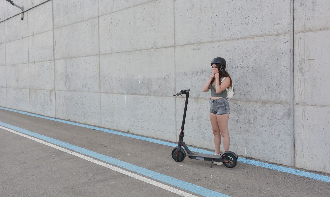 Jeune femme en trottinette électrique assurée en zone urbaine, casque et antivol visibles pour sécurité.