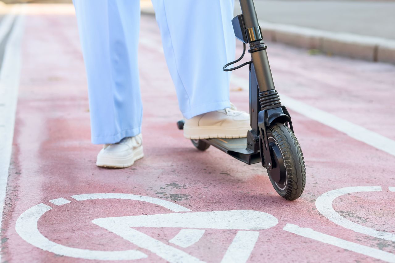 Jeune femme en trottinette électrique sur piste cyclable urbaine, casque visible et circulation fluide.