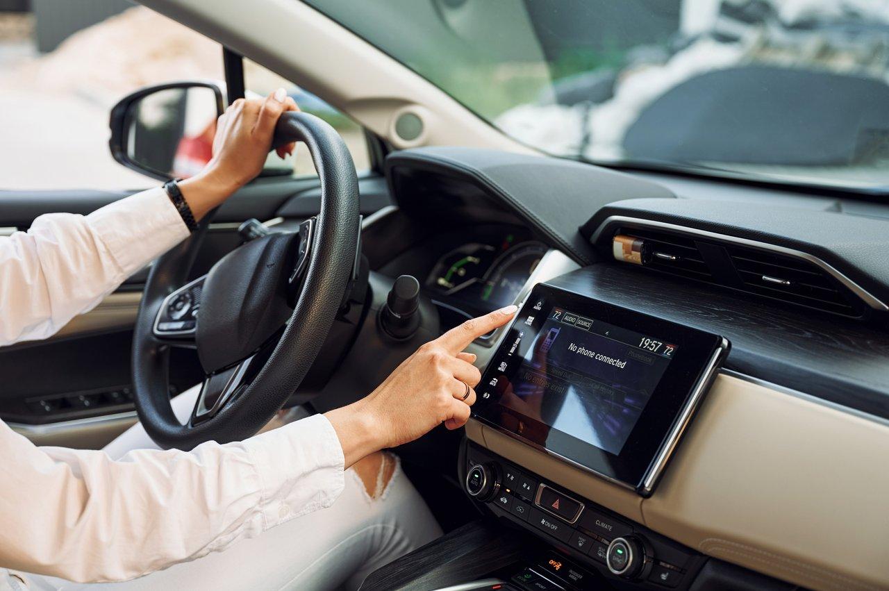Jeune femme utilisant la technologie d’aide à la conduite connectée dans une voiture électrique, illustrant le comparatif des innovations en 2025.