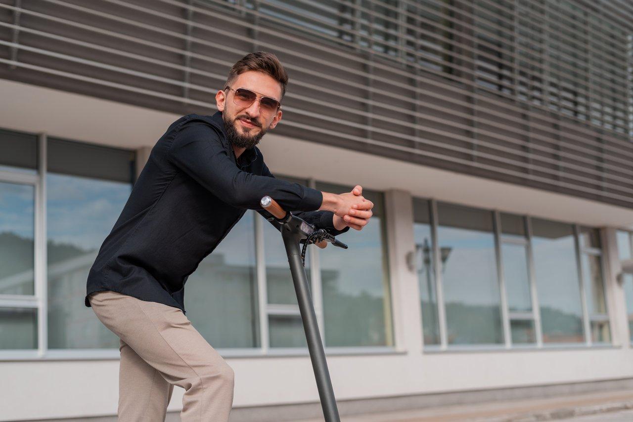Jeune homme portant équipement de sécurité sur un scooter électrique en ville, respectant la limitation de vitesse.