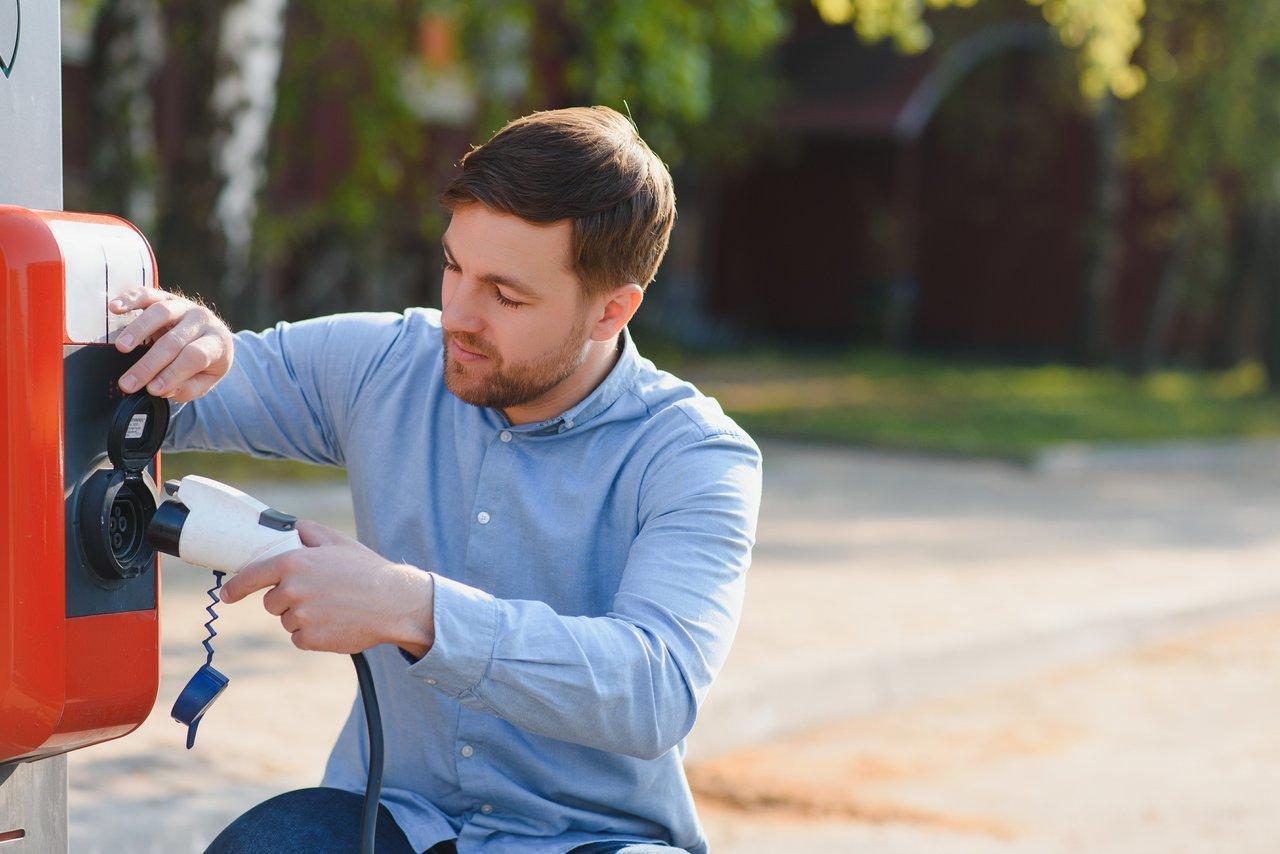 Jeune homme près d’une borne de recharge électrique domestique, illustration de l’assurance pour home electric car charger.