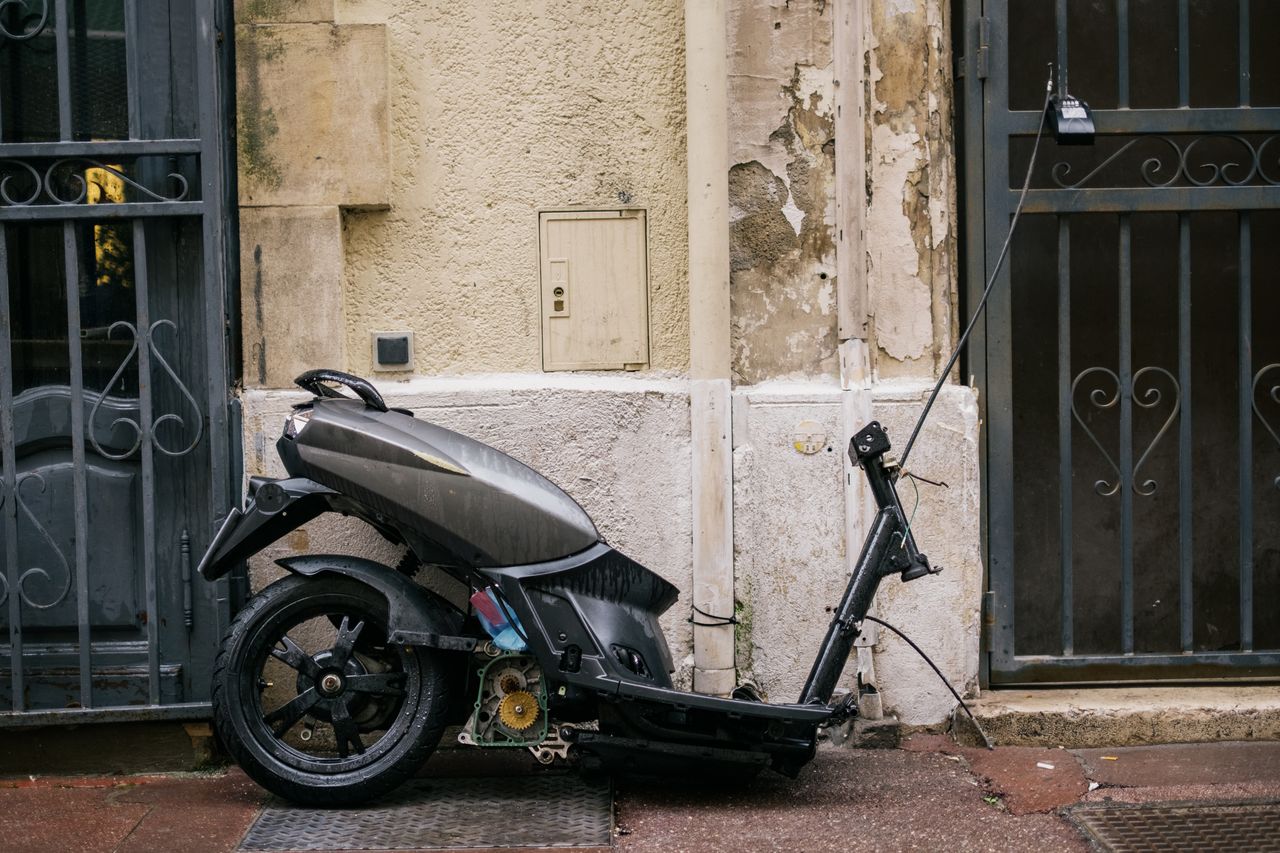 Moto électrique garée en ville près d'une borne de recharge, casque posé, rue urbaine sécurisée.
