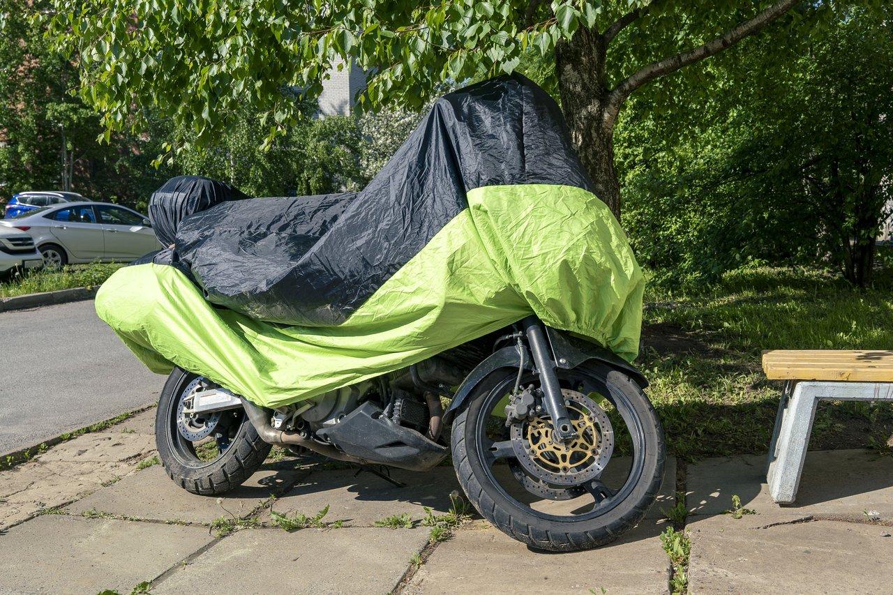 Moto protégée par une housse solide fixée par des sangles dans un espace extérieur.