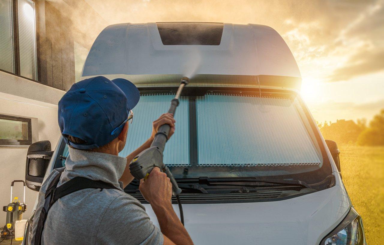 Nettoyage extérieur minutieux d’un RV motorhome au jet d’eau sous la lumière du matin pour préparer l’hivernage.
