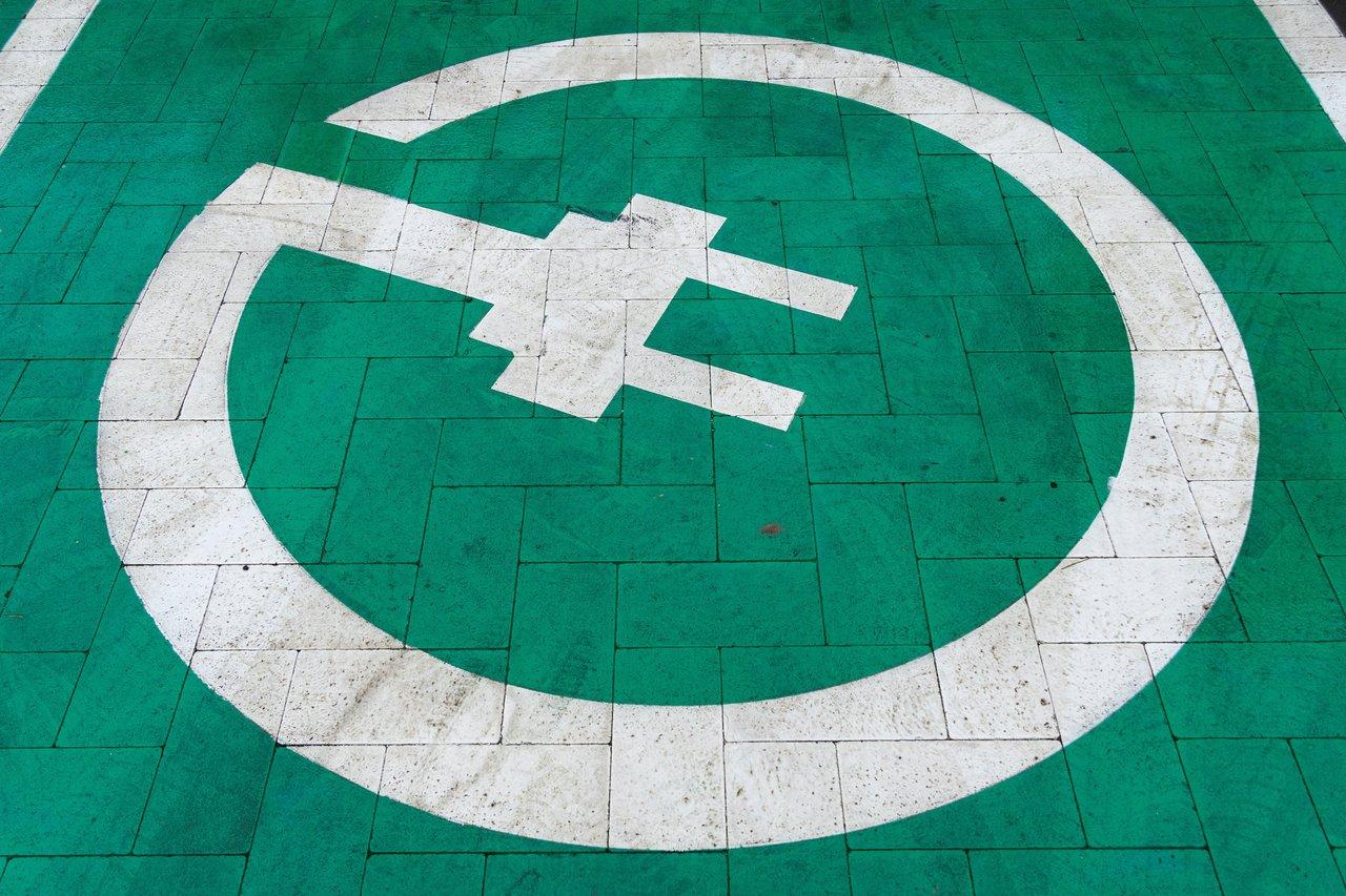 Panneau de prix d'une borne de recharge pour voiture électrique en zone urbaine, illustrant la modernité et les coûts associés.