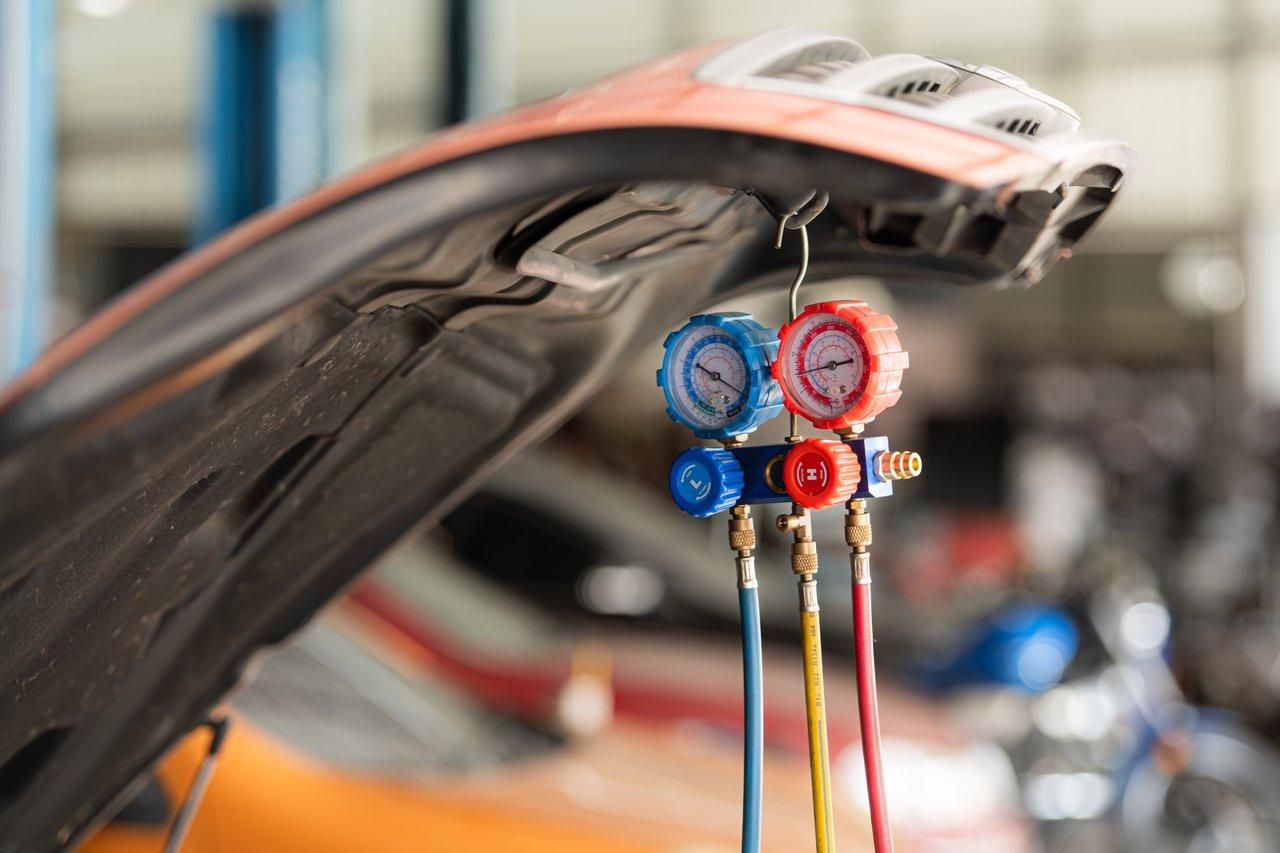 Technicien automobile effectuant une maintenance de la climatisation de voiture avec manomètre et outils spécialisés.