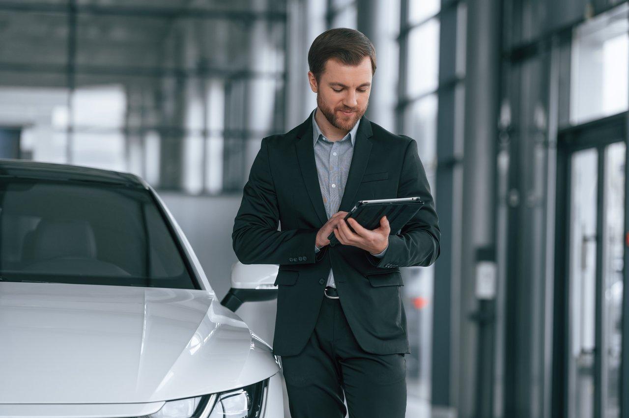 Un homme en costume noir consulte un comparateur de financement auto sur tablette dans une concession automobile.