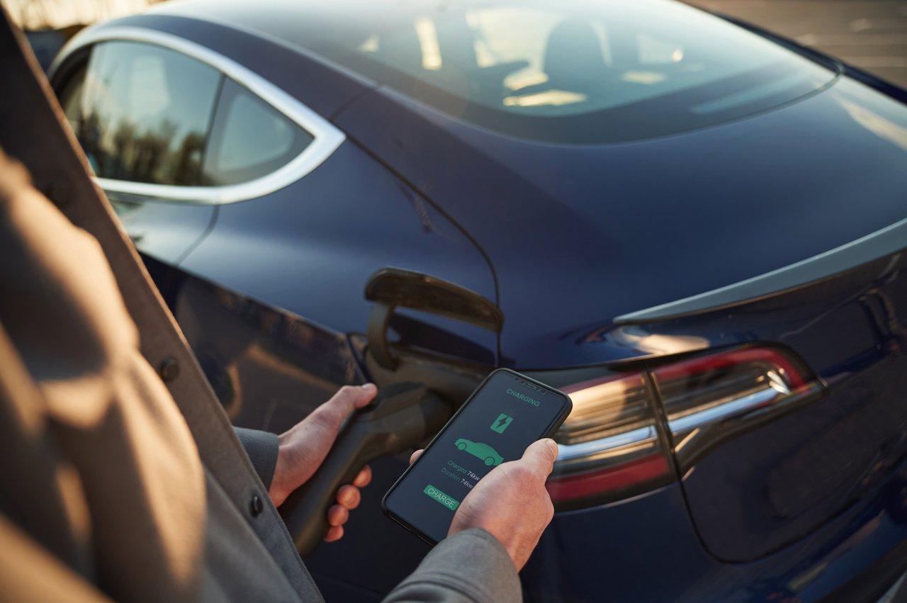Un homme utilise une application de navigation sur smartphone pour optimiser la conduite de sa voiture hybride électrique.