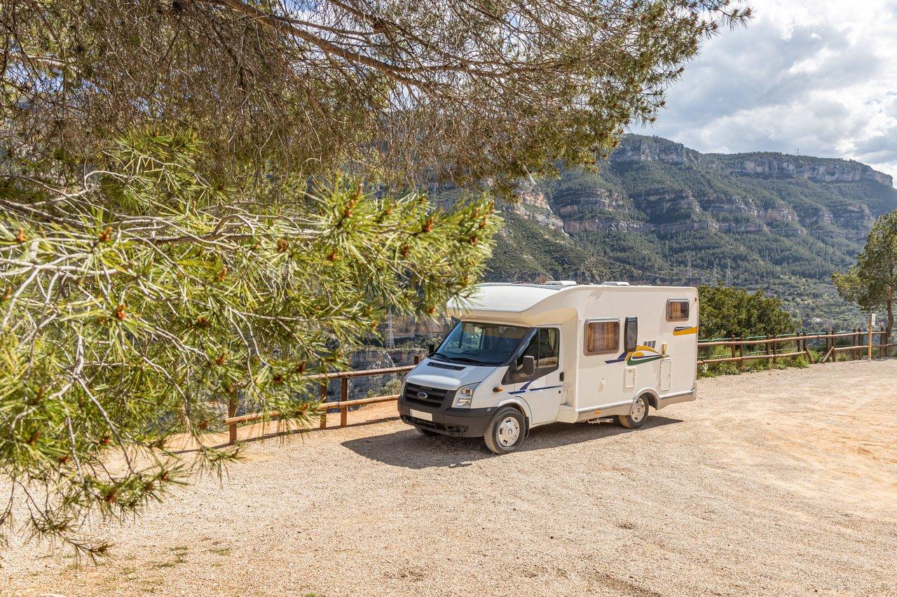 Un motorhome en nature, garé sur un parking offrant un panorama verdoyant idéal pour un séjour abordable.