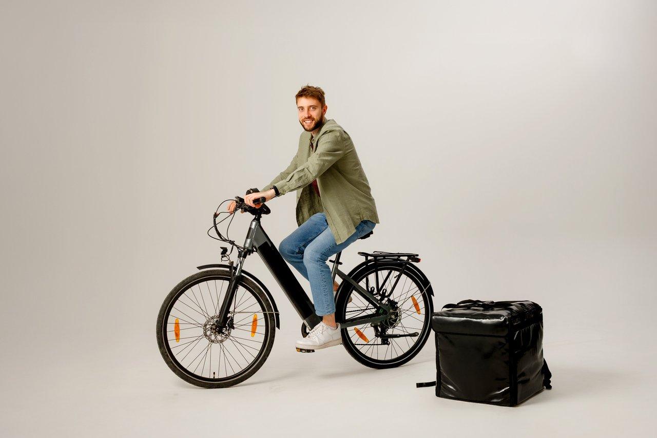 Un utilisateur de modern electric bike en environnement urbain, prêt à livrer avec son vélo électrique et sac isotherme.