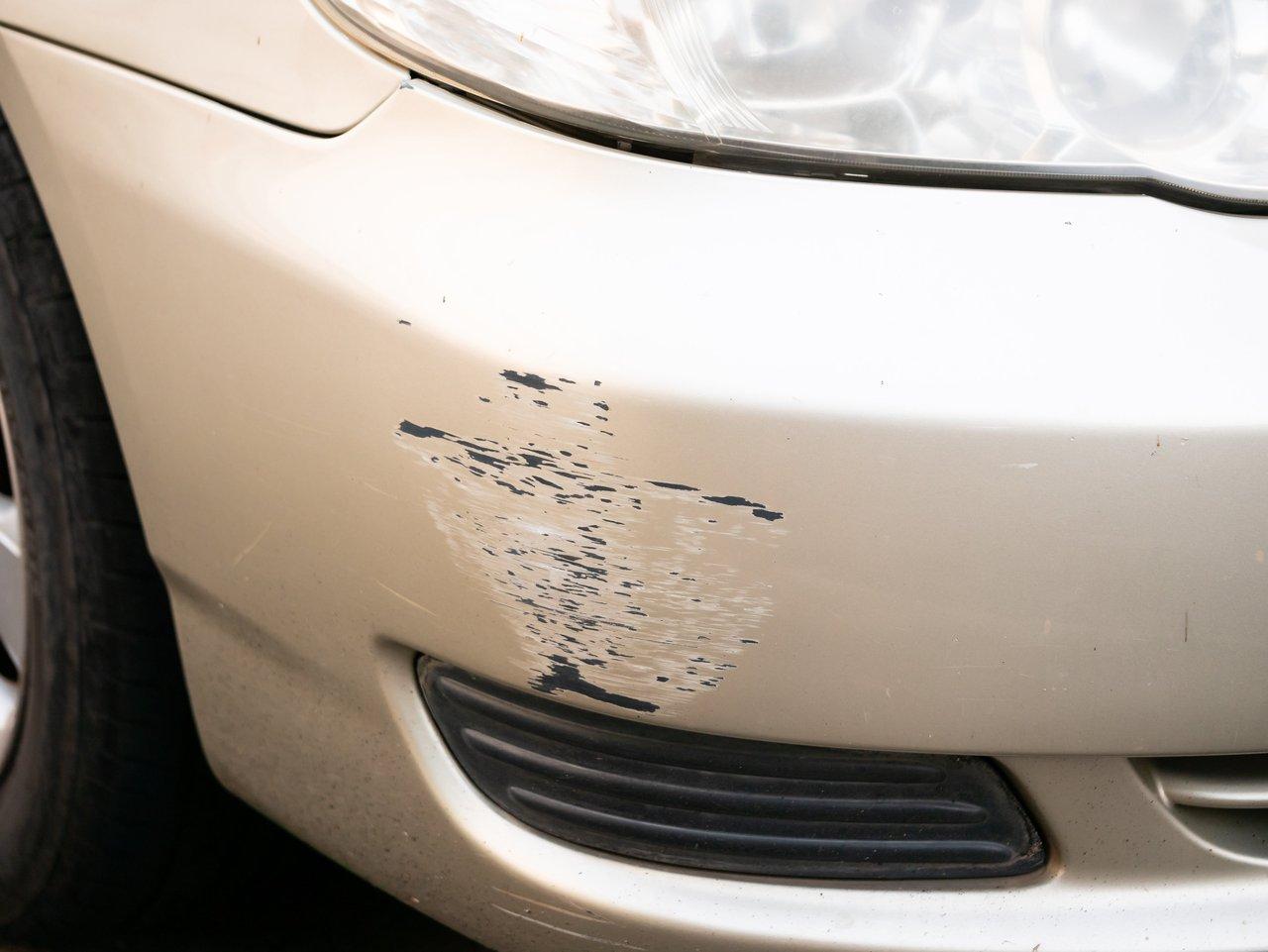 Une main appliquant un rénovateur plastique pour réparer un rayure sur un pare-chocs lors d'une intervention de car bumper scratch repair.