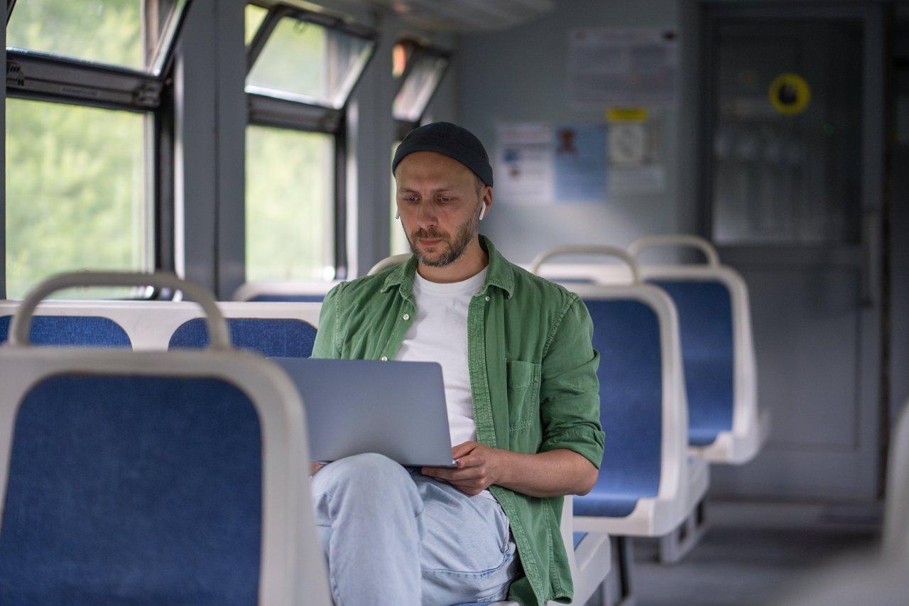 Utilisateur utilisant une application de transport urbain sur son laptop en déplacement en train électrique, pour optimiser ses trajets multimodaux en 2025.