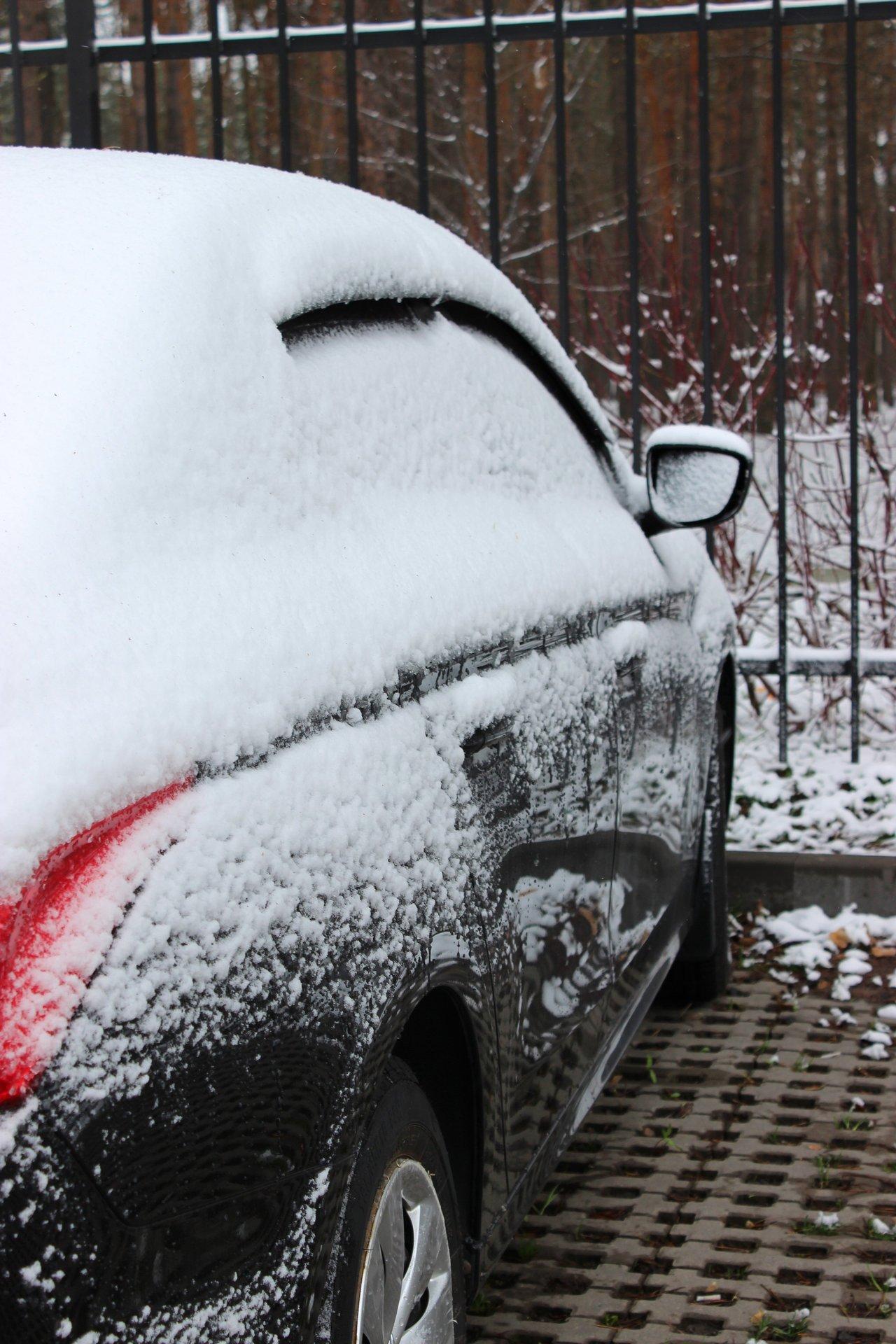 Voiture garée en hiver dans un garage fermé, protégée par une bâche anti-givre sur le capot pour l'entretien.