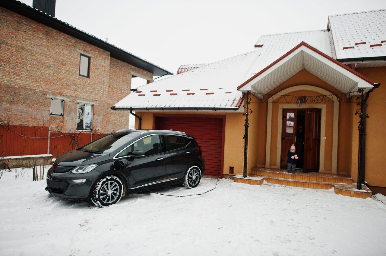 Voiture hybride électrique en charge dans une cour enneigée, idéale pour l’hiver 2025-2026.