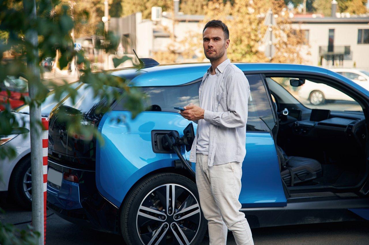 Vue frontale d'un homme avec une voiture hybride électrique à la station de charge, illustrant le contraste entre urban hybrid et petrol cars.